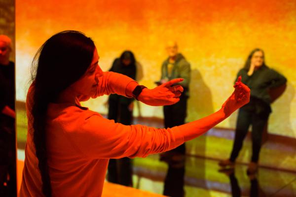 A woman using sign language to communicate with visitors in the FRAMELESS immersive gallery.
