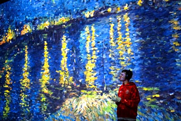 A boy standing in the FRAMELESS immersive gallery listening to the audio guide
